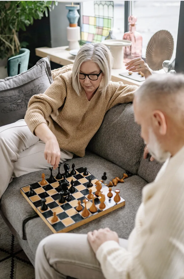 Older adults playing chess together in a bright living room.